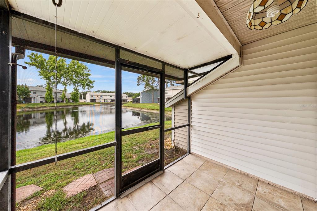 A screened-in patio with tiled flooring overlooks a pond and neighboring residential buildings — 5314 ABINGER COURT, TAMPA, FL