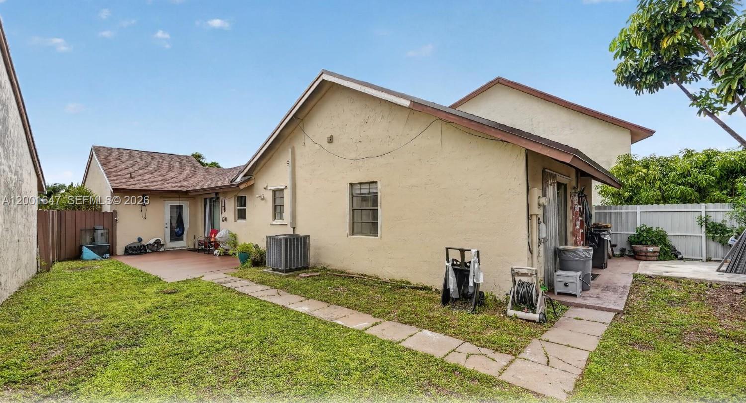 The exterior of a single-story house features a small patio, lawn, and white fencing — 7010 SW 103rd Pl, Miami FL 33173, MIAMI, FL