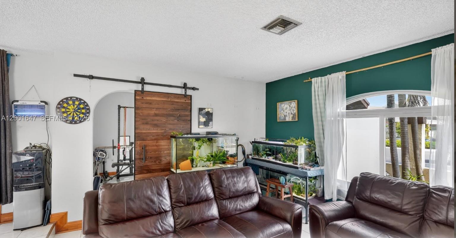 A living room features a dark green accent wall, leather sofas, and two large aquariums — 7010 SW 103rd Pl, Miami FL 33173, MIAMI, FL