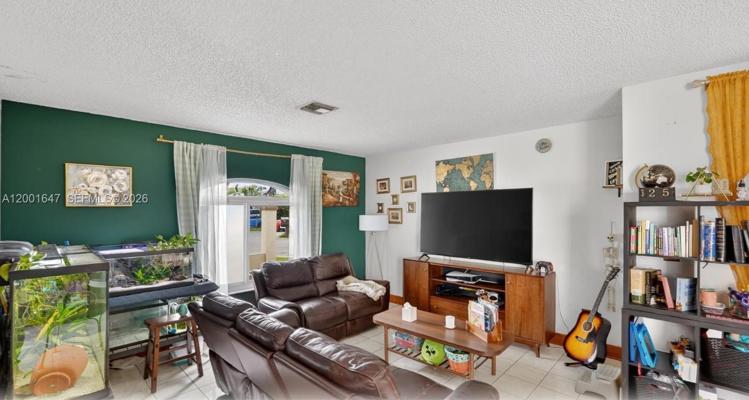 A living room features a green accent wall, brown leather sofas, a television, and bookshelves — 7010 SW 103rd Pl, Miami FL 33173, MIAMI, FL