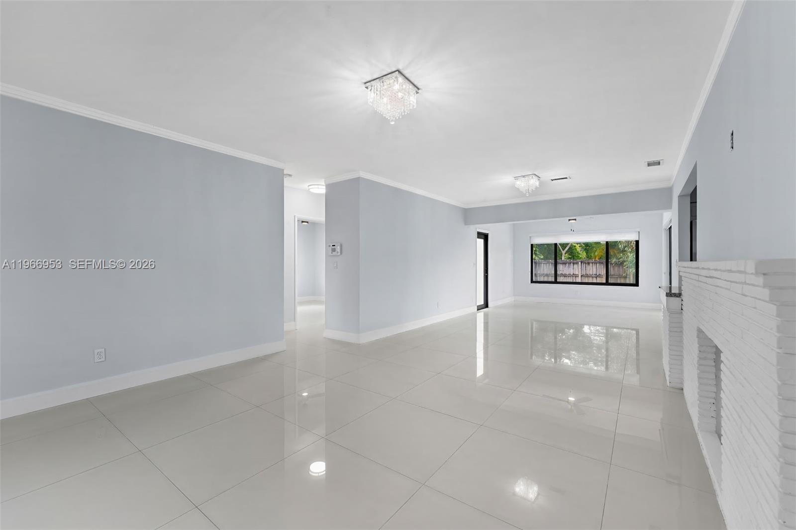 A bright, open living room features white tile floors, light blue walls, and two crystal chandeliers — 1998 NE 180th St, North Miami Beach FL 33162, NORTH MIAMI BEACH, FL