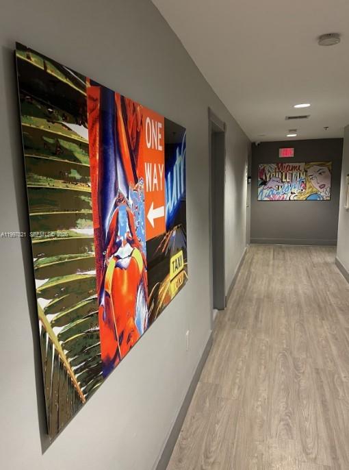 A hallway features light wood-look flooring and two large, colorful art pieces on the walls — 335 Ocean Dr # 214, Miami Beach FL 33139, MIAMI BEACH, FL