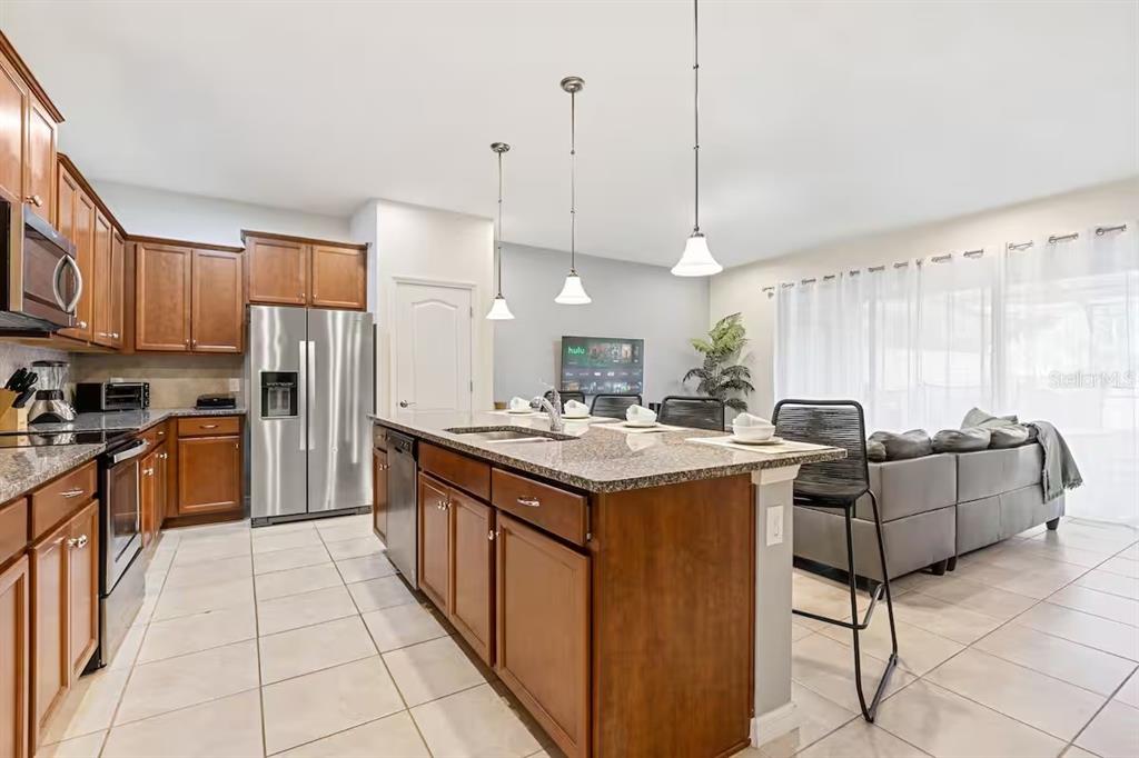 A kitchen with wood cabinets, granite countertops, and a large island opens to a living area — 2402 DUBAI STREET, KISSIMMEE, FL