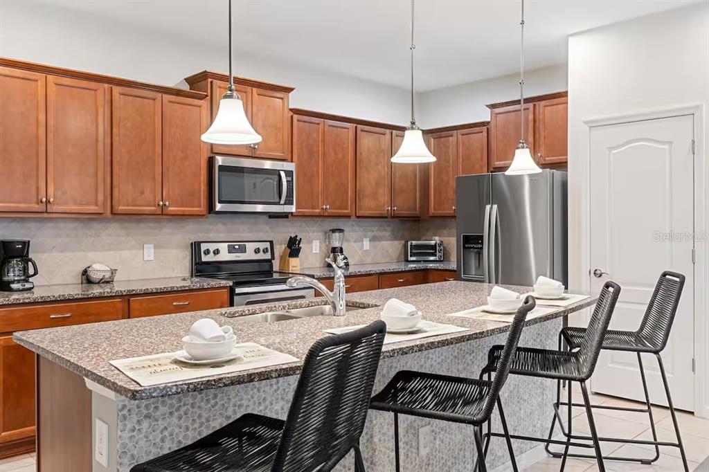 A kitchen with wood cabinets, granite countertops, a center island with bar seating, and stainless appliances — 2402 DUBAI STREET, KISSIMMEE, FL