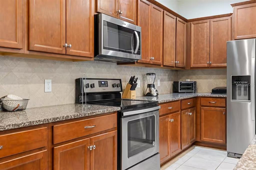 A kitchen features wood cabinets, stainless steel appliances, and granite countertops — 2402 DUBAI STREET, KISSIMMEE, FL