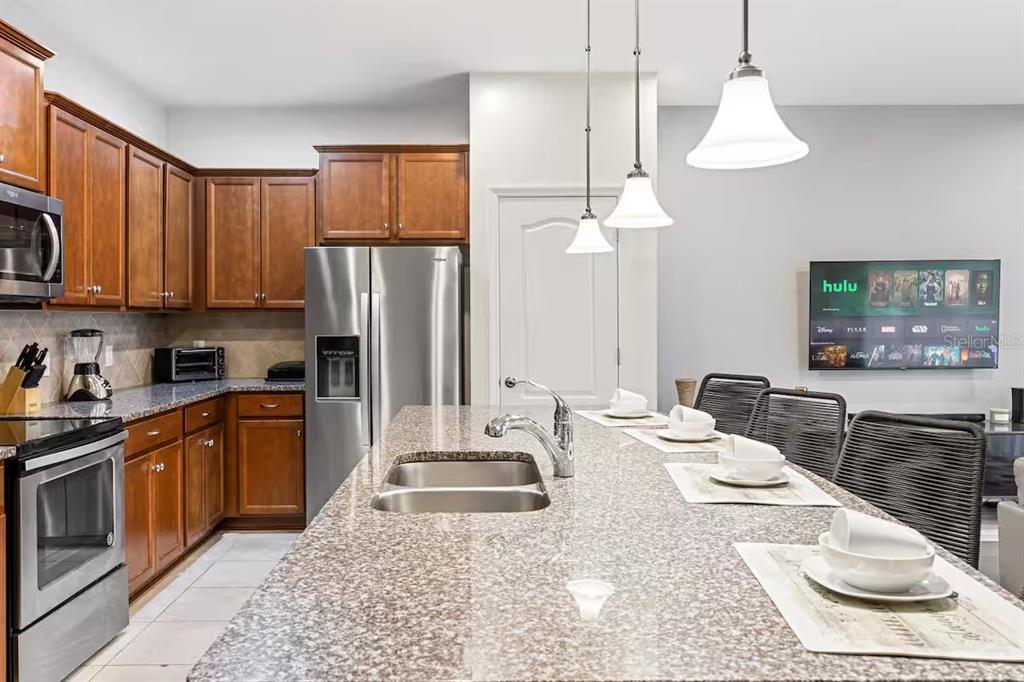 A kitchen features wood cabinets, granite countertops, a stainless steel refrigerator, and a breakfast island — 2402 DUBAI STREET, KISSIMMEE, FL