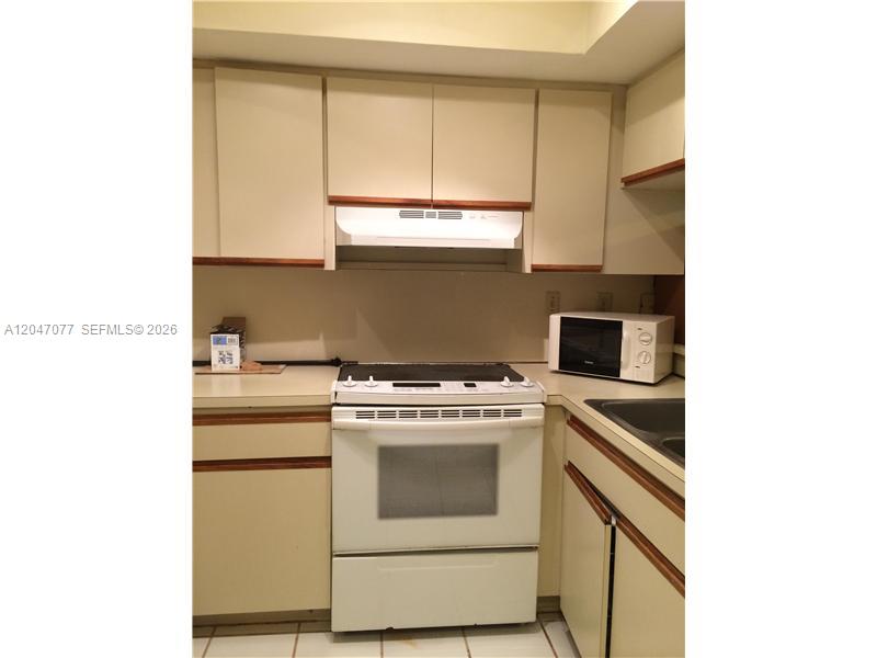 A kitchen features white appliances, light-colored cabinets with wood trim, and a tiled floor — 8977 SW 123rd Ct # 202, Miami FL 33186, MIAMI, FL