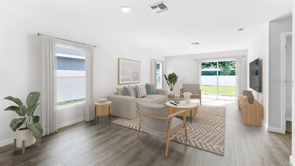 This virtually staged living room features light wood-look flooring, white walls, and a sliding glass door — 5168 SCHUBERT TRAIL, NORTH PORT, FL