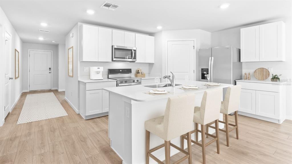 A modern kitchen features white cabinets, stainless steel appliances, and a central island with seating — 5168 SCHUBERT TRAIL, NORTH PORT, FL