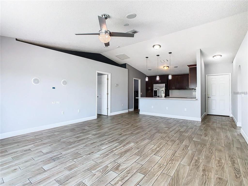 An open-concept living room features wood-look tile flooring, a ceiling fan, and a kitchen island — 3194 WINDMILL POINT BOULEVARD, KISSIMMEE, FL