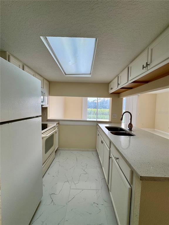 A kitchen features white cabinets, a light-colored countertop, a double sink, and marble-patterned floor tiles — 425 CARIBBEAN DRIVE, DAVENPORT, FL