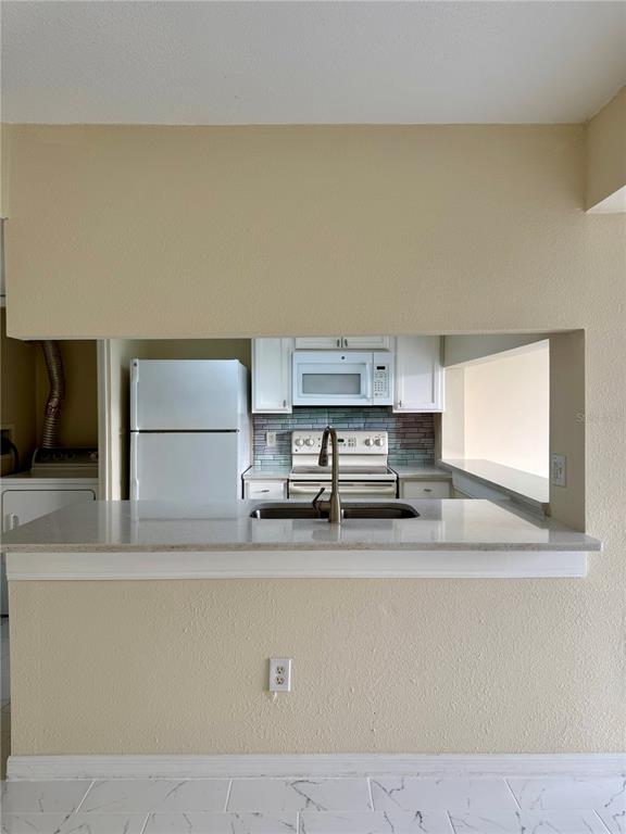 A kitchen features white cabinets, a pass-through window, and a breakfast bar with stone countertops — 425 CARIBBEAN DRIVE, DAVENPORT, FL