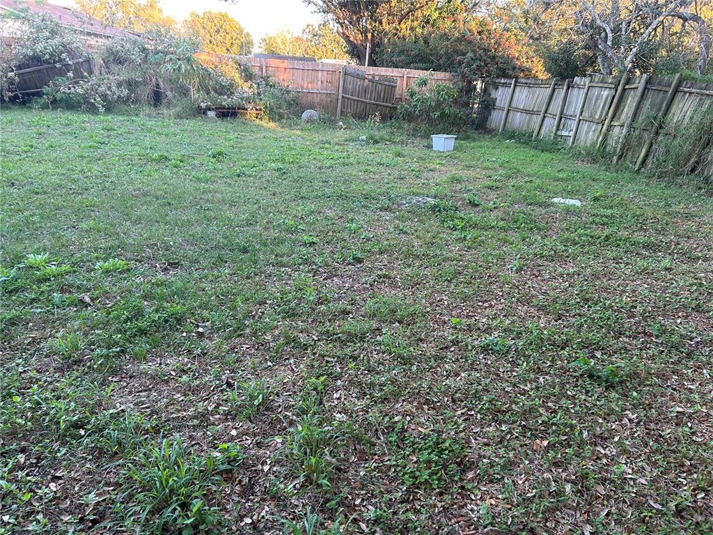 A grassy backyard features a wooden fence, scattered leaves, and some overgrown vegetation — 5391 BOTANY COURT, ORLANDO, FL