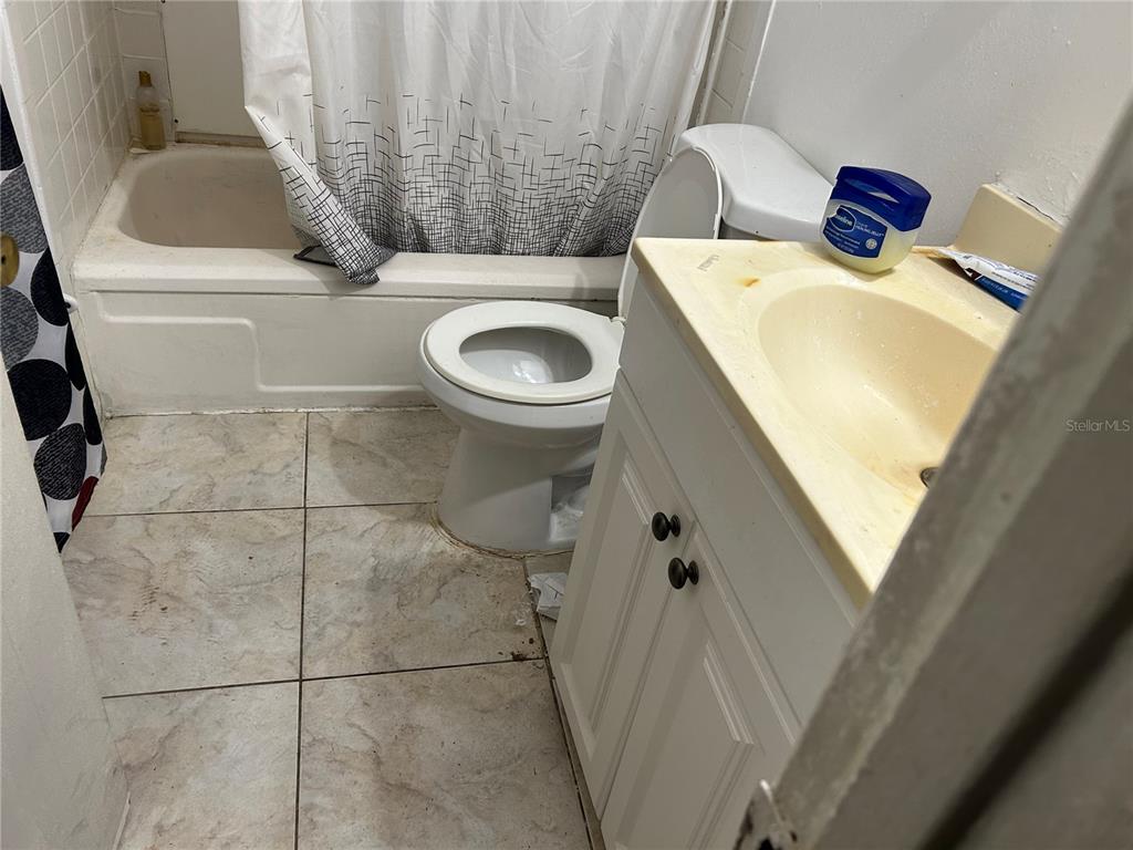 A small bathroom features a white vanity, a toilet, and a bathtub with a shower curtain — 5391 BOTANY COURT, ORLANDO, FL