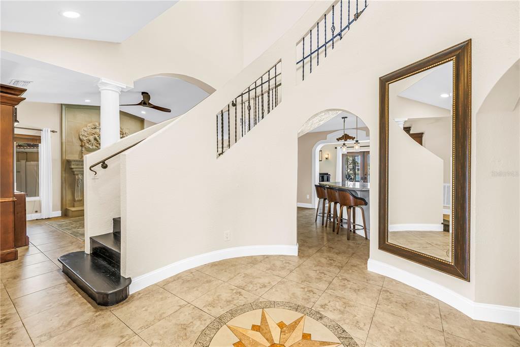 A curved staircase with black treads and iron railings stands in a tiled foyer — 3945 POINSETTIA DRIVE, ST PETE BEACH, FL