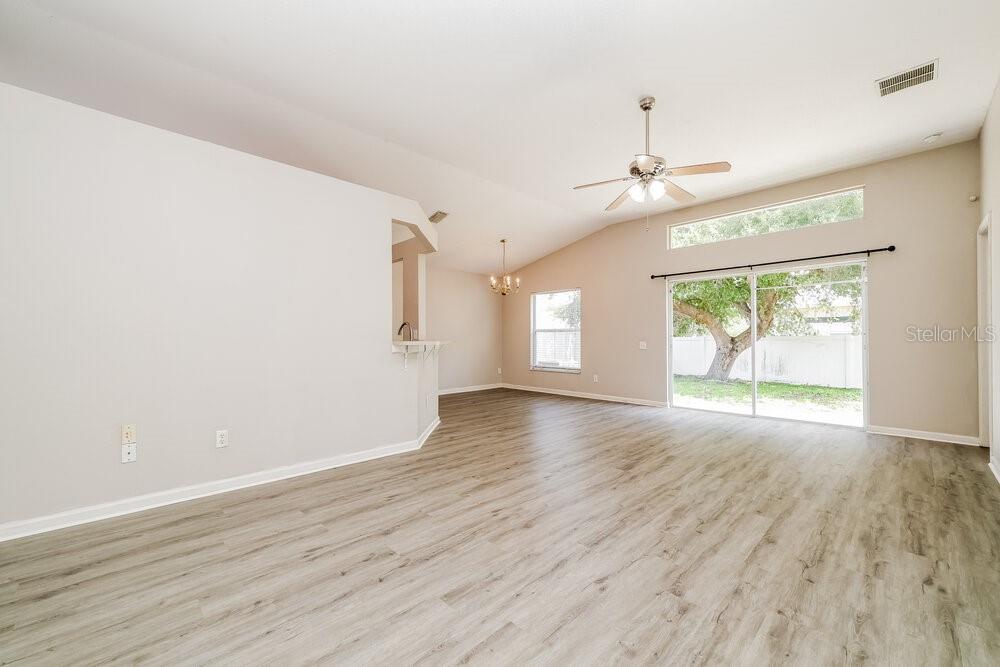 An empty living room features light wood-look flooring, vaulted ceilings, and a sliding glass door — 10422 HUNTERS HAVEN BOULEVARD, RIVERVIEW, FL
