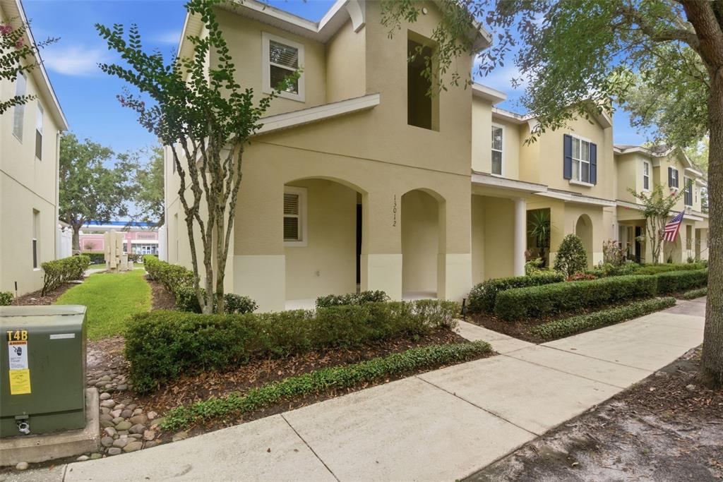 A two-story tan townhouse with a covered entryway and manicured hedges along the sidewalk — 13012 AUBURN COVE LN, ORLANDO, FL