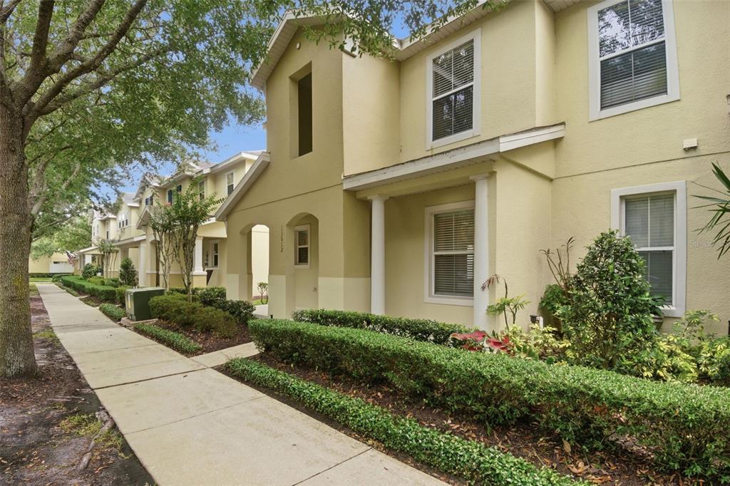 A two-story tan townhouse with a sidewalk, manicured hedges, and white columns at the entrance — 13012 AUBURN COVE LN, ORLANDO, FL