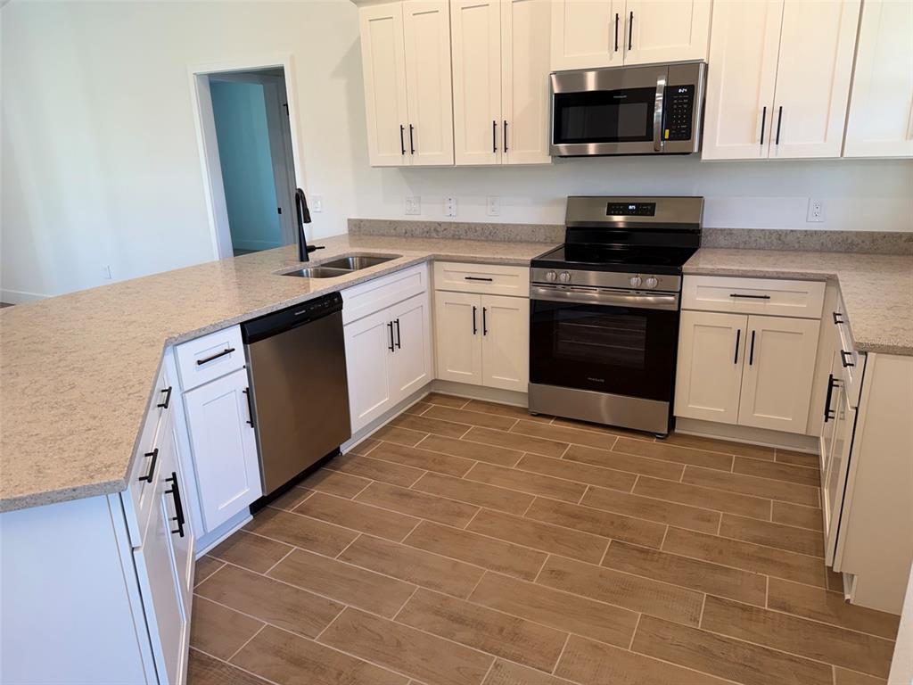 A kitchen with white cabinets, stainless steel appliances, and light-colored countertops over wood-look tile flooring — 1252 FLEETWOOD DRIVE, PORT CHARLOTTE, FL
