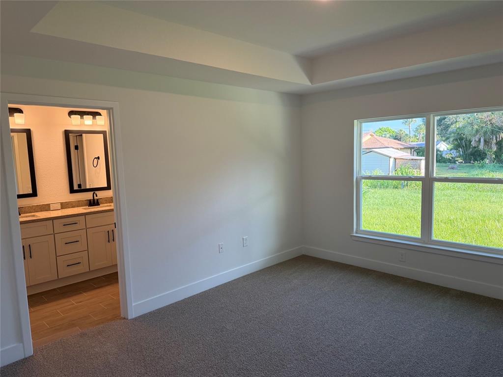 A bedroom with gray carpet and a tray ceiling leads into an attached bathroom — 1252 FLEETWOOD DRIVE, PORT CHARLOTTE, FL