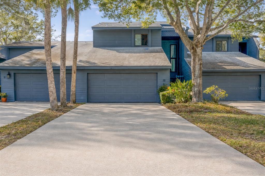 A multi-story house exterior at dusk with a stone patio, landscaping, and illuminated balconies — 12 MARINER DRIVE UNIT 12, TARPON SPRINGS, FL