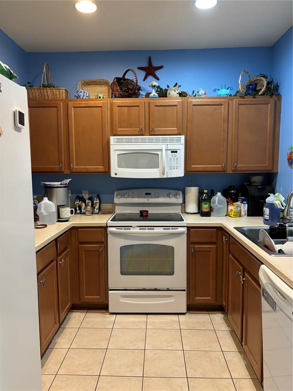 A kitchen features wood cabinets, white appliances, a blue wall, and tile flooring — 3825 45TH TERRACE W UNIT 104, BRADENTON, FL