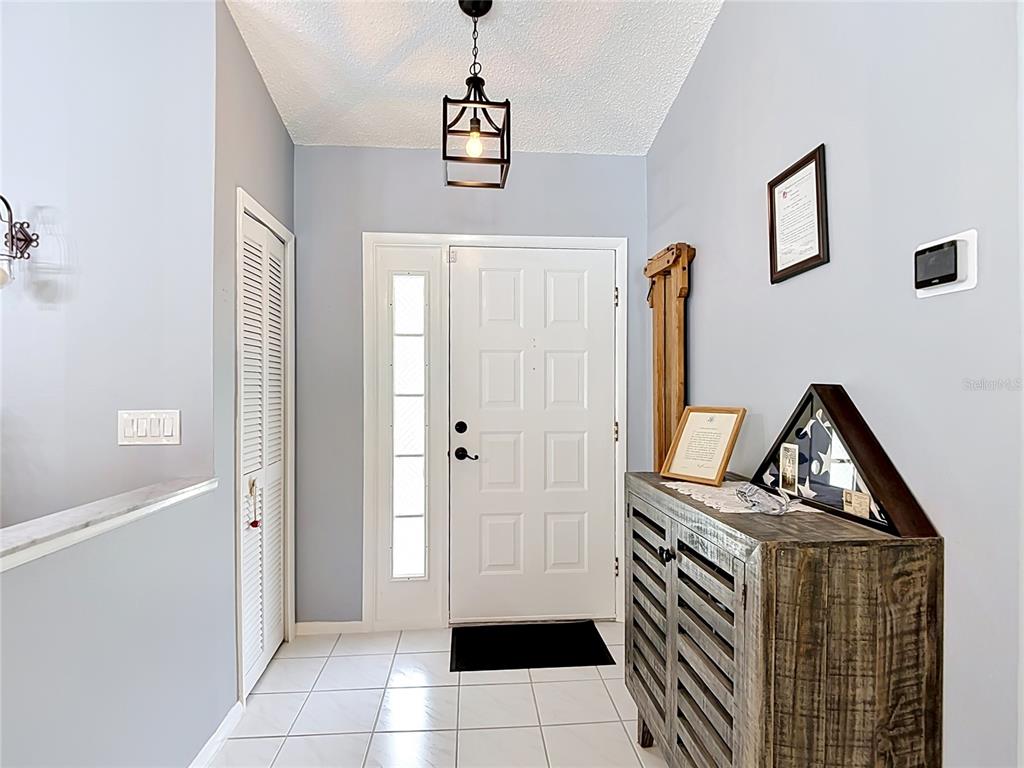 An entryway features a white front door, tiled floors, a pendant light, and a wooden cabinet — 11382 PICKFORD STREET, SPRING HILL, FL