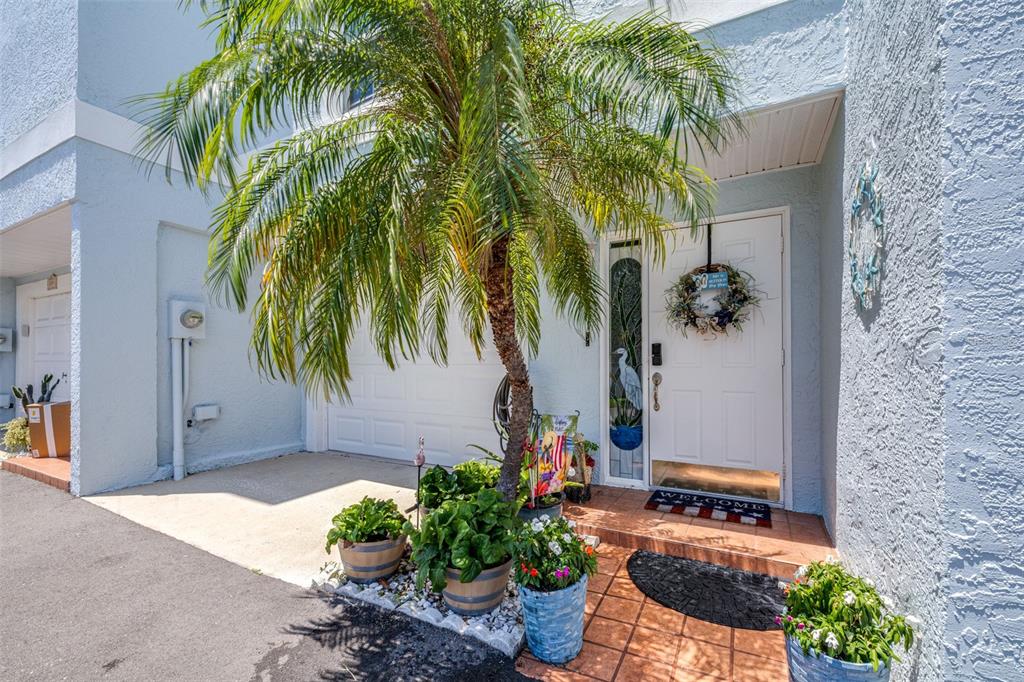 A palm tree stands in front of a white front door with a decorative wreath — 751 PINELLAS BAYWAY S UNIT 208, TIERRA VERDE, FL