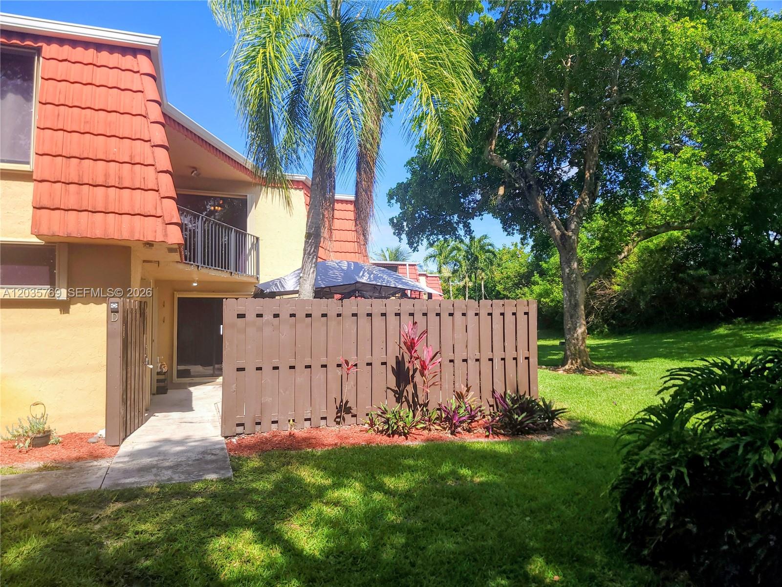 A brown wooden fence encloses a patio area next to a building with red roof tiles — 23106 Oxford Pl # D, Boca Raton FL 33433, BOCA RATON, FL