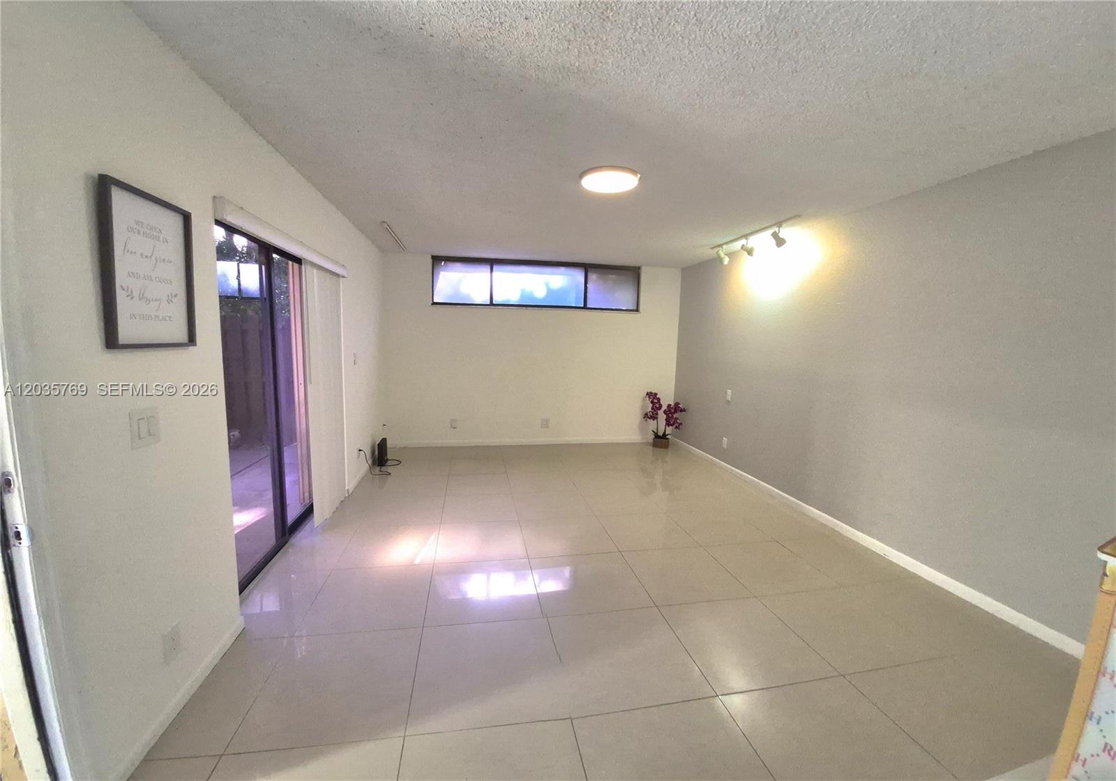 An empty room features light-colored tile flooring, a sliding glass door, and a horizontal window — 23106 Oxford Pl # D, Boca Raton FL 33433, BOCA RATON, FL