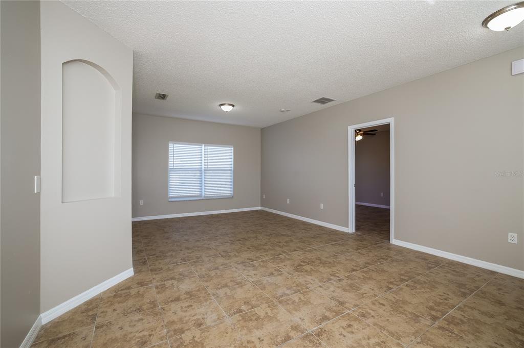 An empty room with beige walls, tile flooring, a recessed wall niche, and a window — 446 SPIKE COURT, KISSIMMEE, FL