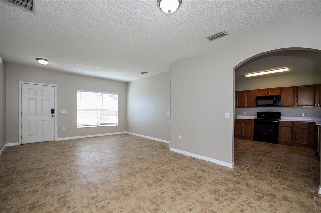 An open-concept living area with tile flooring leads into a kitchen through an arched doorway — 446 SPIKE COURT, KISSIMMEE, FL