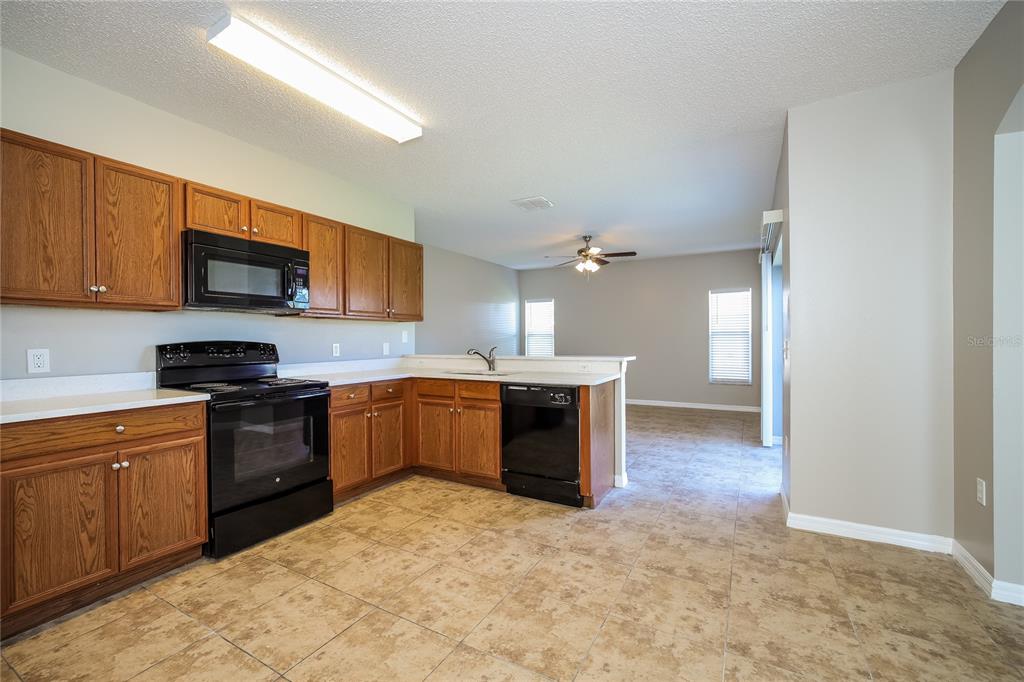 A kitchen with wood cabinets, black appliances, and tile flooring opens to a living area — 446 SPIKE COURT, KISSIMMEE, FL