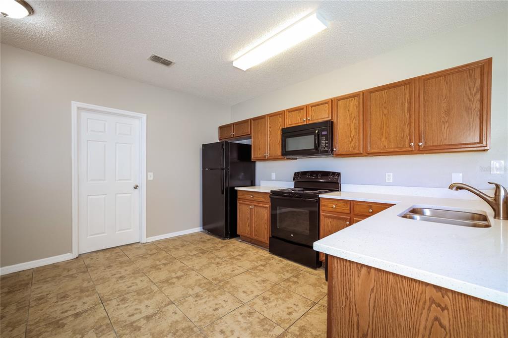 A kitchen with oak cabinets, black appliances, white countertops, and tan tile flooring — 446 SPIKE COURT, KISSIMMEE, FL