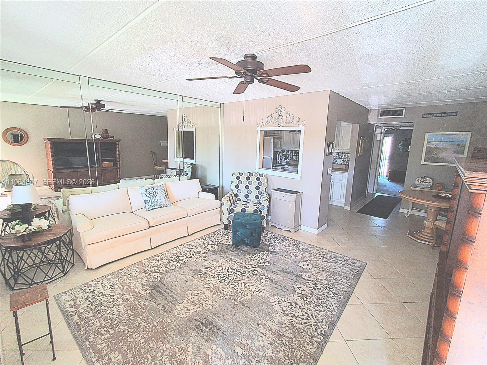 A living room features a white sofa, patterned armchair, large area rug, and mirrored wall — 3000 Springdale Blvd # V207, Palm Springs FL 33461, PALM SPRINGS, FL
