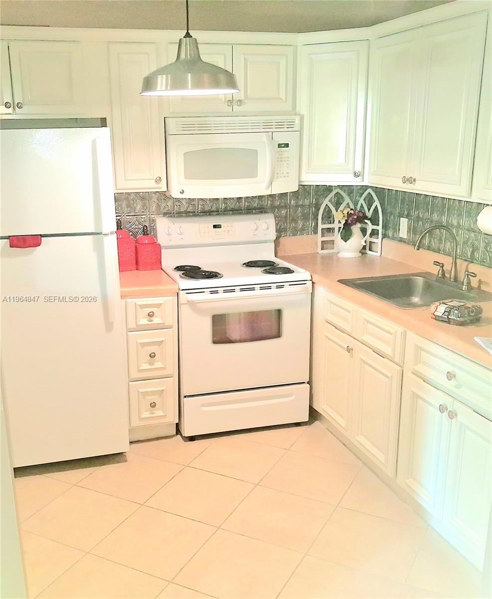 A kitchen features white cabinets, a white stove, a refrigerator, and light-colored countertops — 3000 Springdale Blvd # V207, Palm Springs FL 33461, PALM SPRINGS, FL
