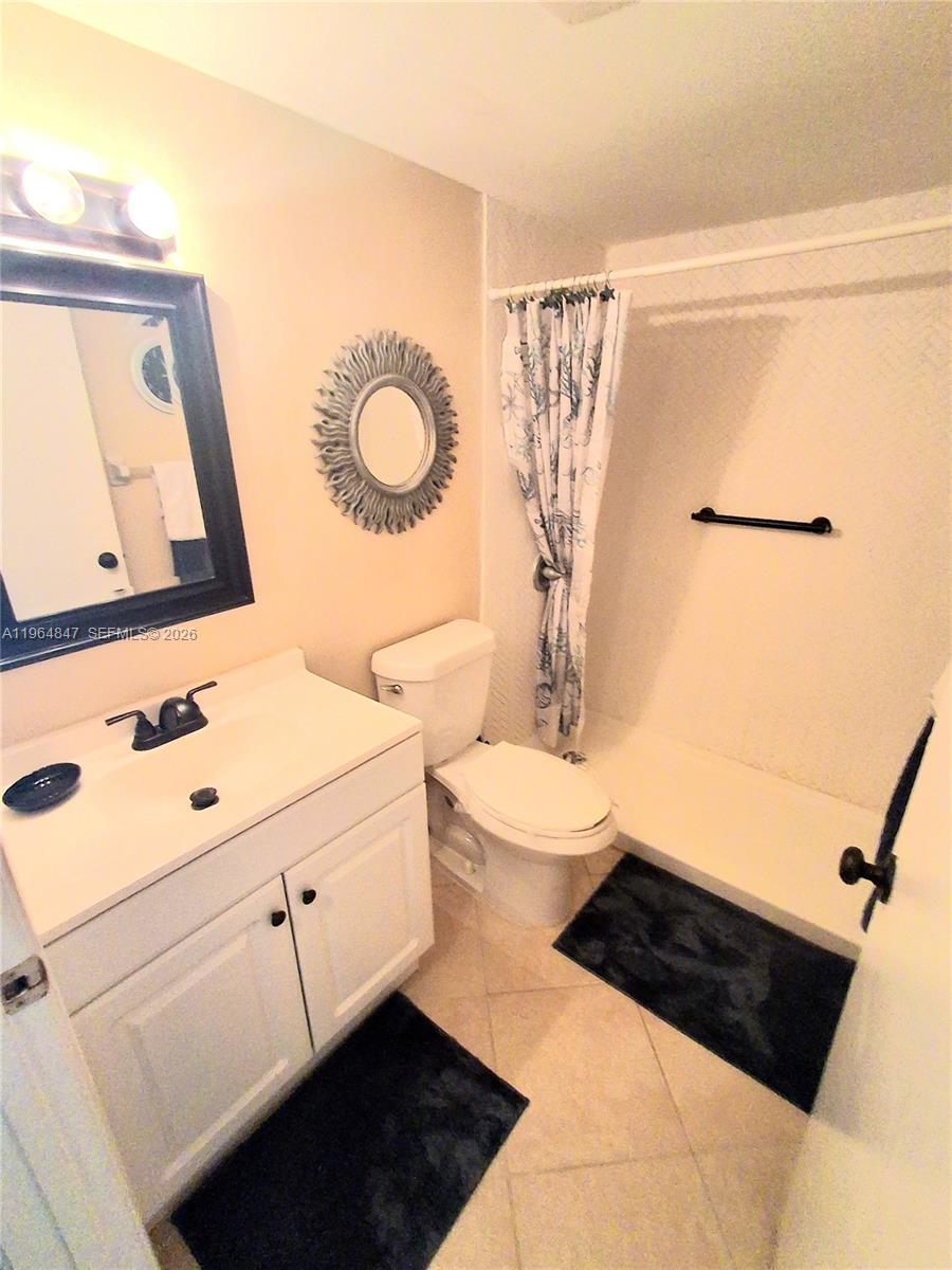 A bathroom features a white vanity, a toilet, and a shower with a patterned curtain — 3000 Springdale Blvd # V207, Palm Springs FL 33461, PALM SPRINGS, FL