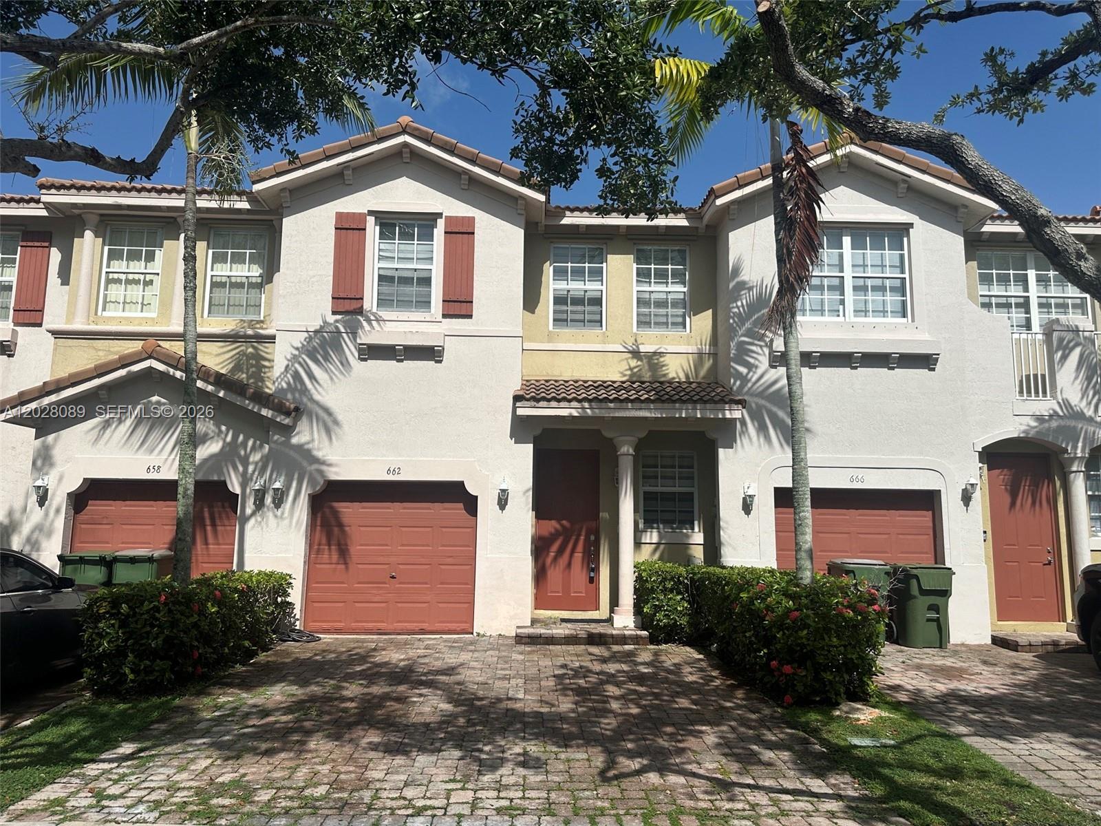 A row of three-story townhouses features beige stucco walls, red garage doors, and brick driveways — 662 NE 21st Ter, Homestead FL 33033, HOMESTEAD, FL