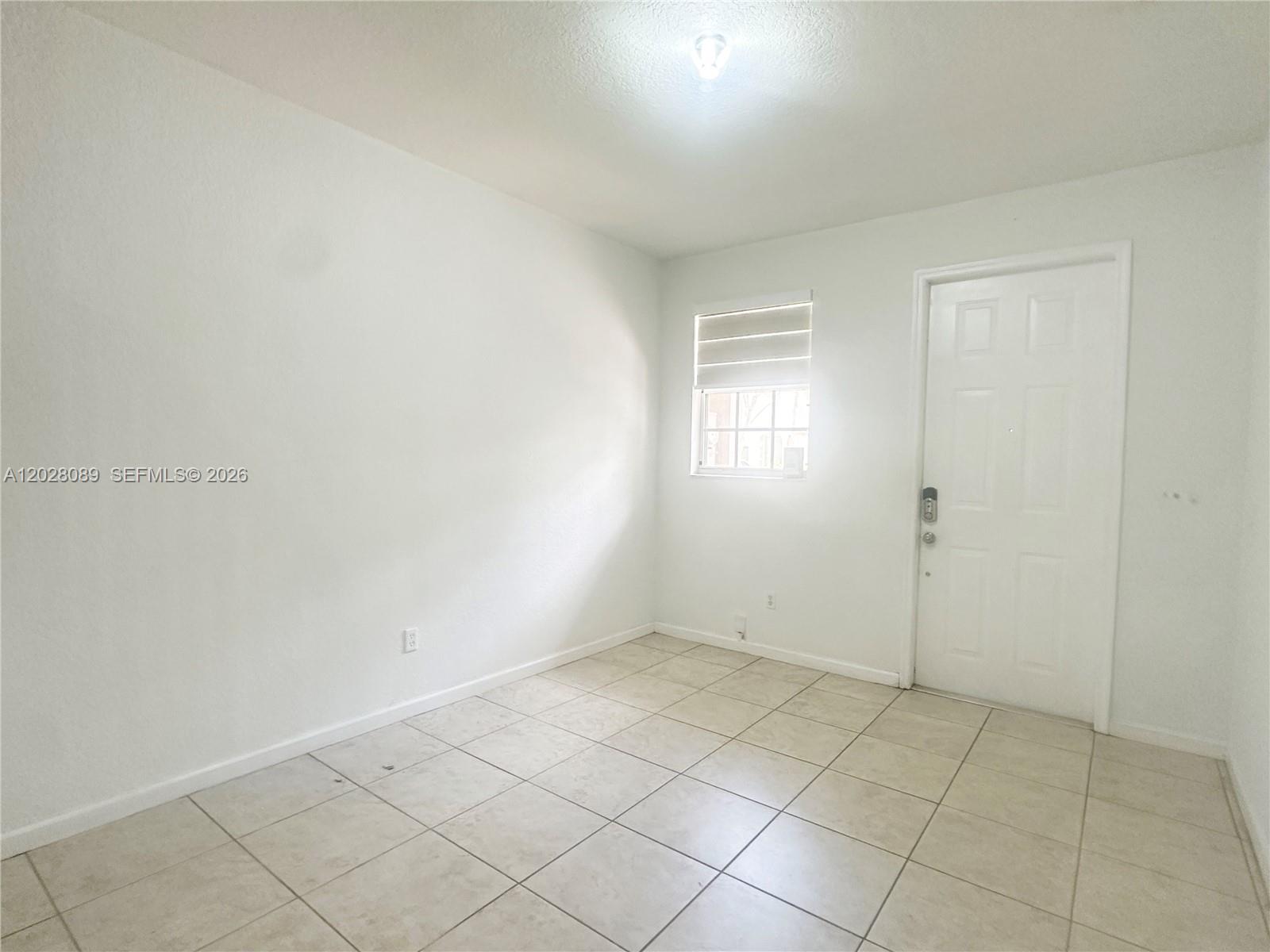 An empty room features white walls, light-colored tile flooring, a single window, and a door — 662 NE 21st Ter, Homestead FL 33033, HOMESTEAD, FL