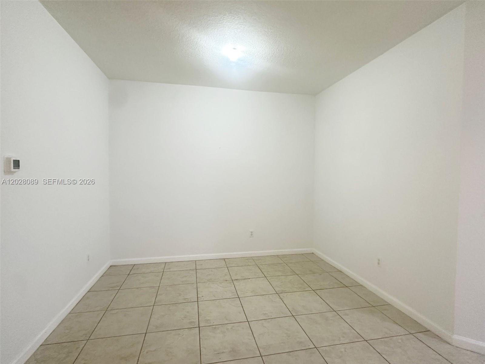 An empty room features white walls, a light-colored tiled floor, and a ceiling light fixture — 662 NE 21st Ter, Homestead FL 33033, HOMESTEAD, FL