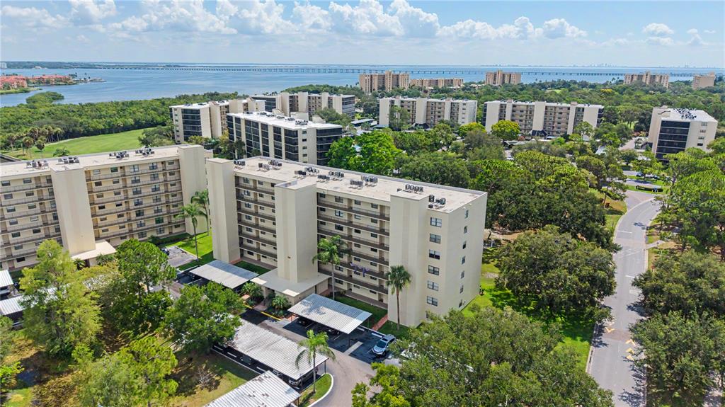 An aerial view shows several multi-story apartment buildings surrounded by trees and parking structures — 800 COVE CAY DRIVE UNIT 5G, CLEARWATER, FL