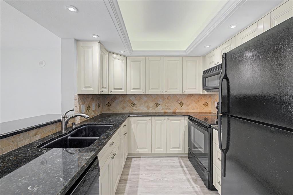 A kitchen with cream cabinets, dark granite countertops, black appliances, and a tiled backsplash — 800 COVE CAY DRIVE UNIT 5G, CLEARWATER, FL