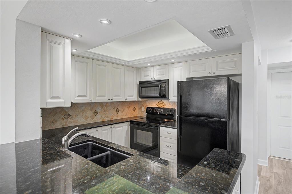 A kitchen with white cabinets, dark granite countertops, black appliances, and a tiled backsplash — 800 COVE CAY DRIVE UNIT 5G, CLEARWATER, FL