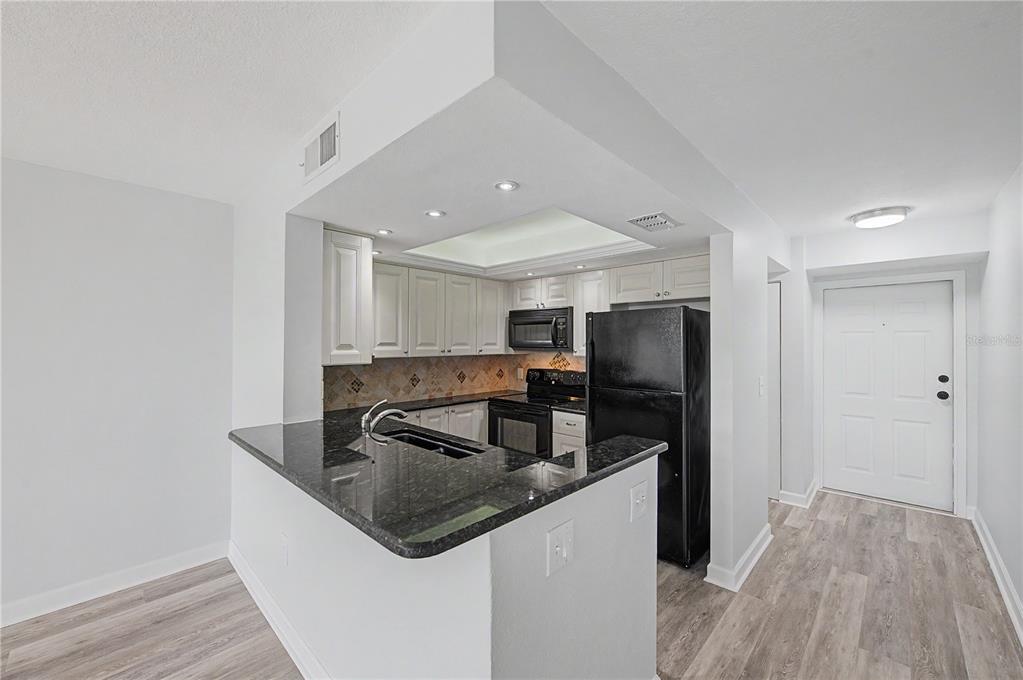 A kitchen features white cabinets, black appliances, and a dark granite countertop breakfast bar — 800 COVE CAY DRIVE UNIT 5G, CLEARWATER, FL