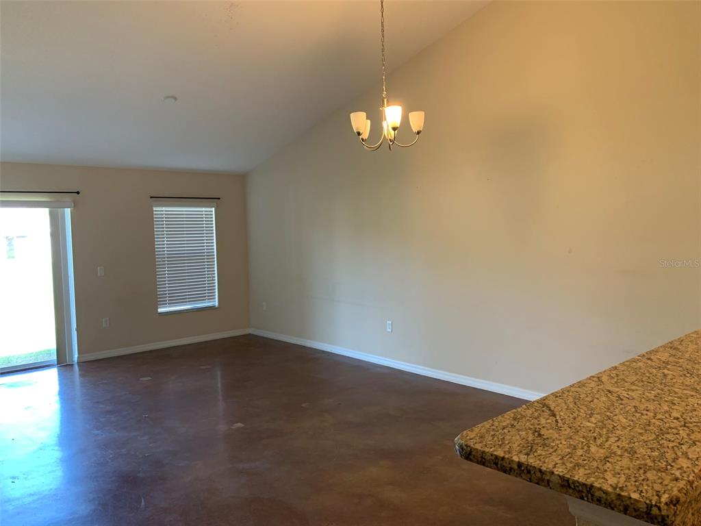 An empty room features a vaulted ceiling, a chandelier, and stained concrete floors — 700 DAKOTA AVENUE, ST CLOUD, FL