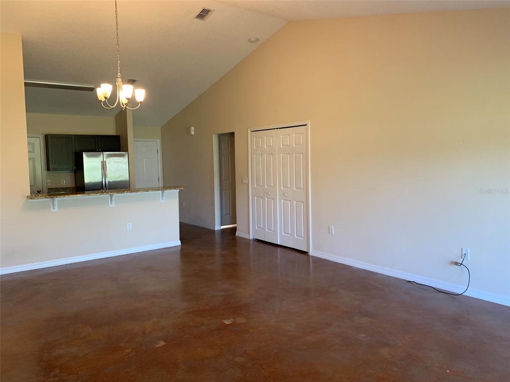 A living room with stained concrete floors, a vaulted ceiling, and an open kitchen area — 700 DAKOTA AVENUE, ST CLOUD, FL