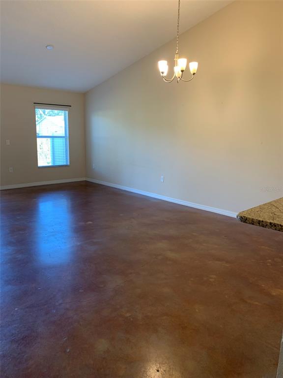 An empty room with stained concrete floors, a vaulted ceiling, and a hanging chandelier — 700 DAKOTA AVENUE, ST CLOUD, FL