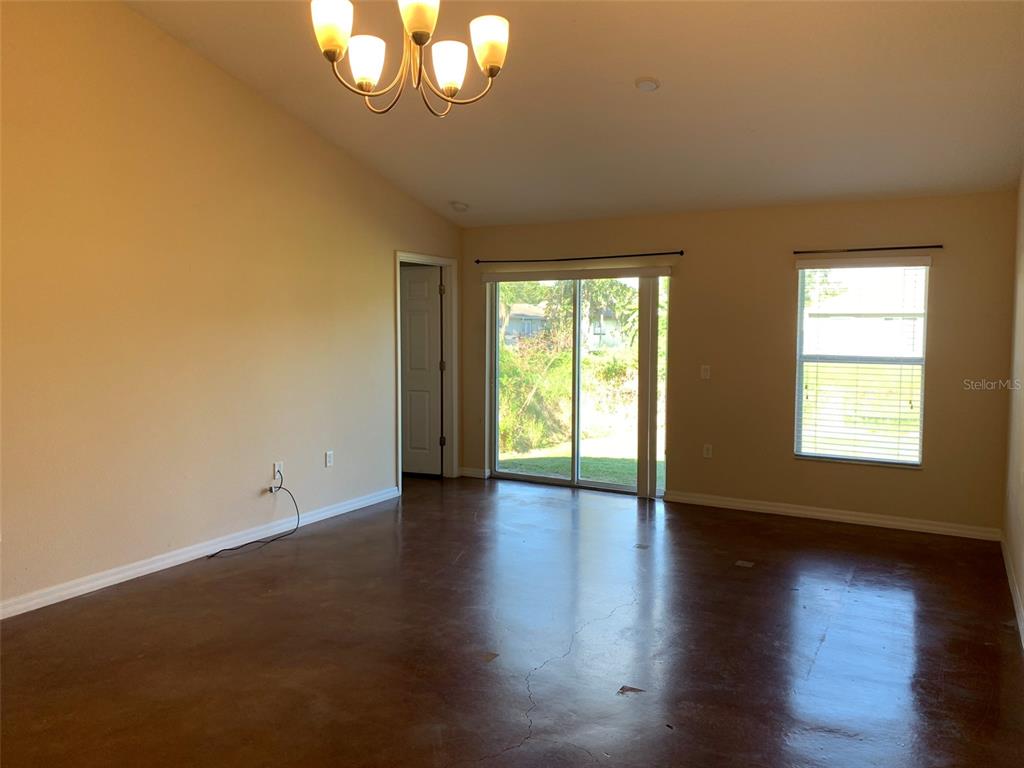 A living room features a vaulted ceiling, a chandelier, sliding glass doors, and concrete floors — 700 DAKOTA AVENUE, ST CLOUD, FL