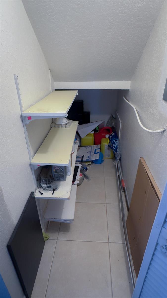 A small, narrow storage closet features white walls, tiled flooring, and open wall-mounted shelving — 407 Arabian Road, Palm Springs FL 33461, PALM SPRINGS, FL