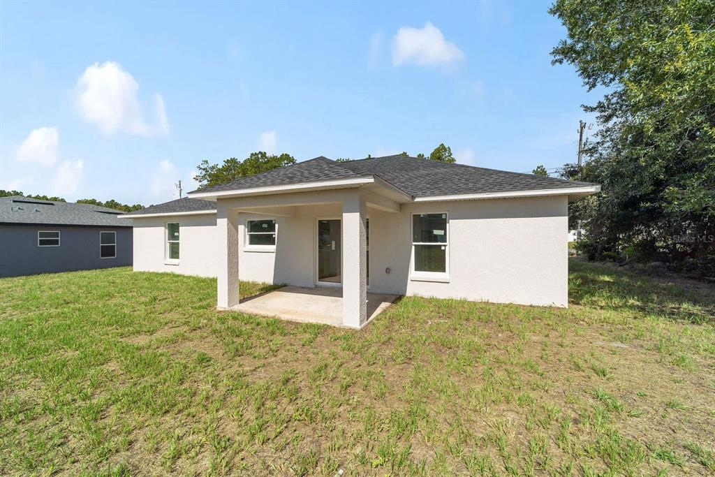The exterior of a single-story house features a covered concrete patio and a grassy yard — 7536 SW 129TH PLACE, OCALA, FL